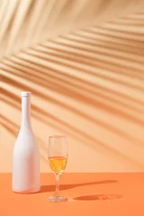 Poster Top view of tropical leaf shadow, white bottle and wine glass on orange background. Summer tropical celebration party. © Creative Photo Focus