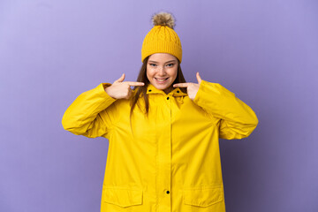 Teenager girl wearing a rainproof coat over isolated purple background giving a thumbs up gesture