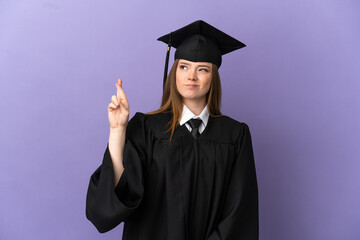 Young university graduate over isolated purple background with fingers crossing and wishing the best