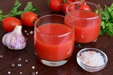 tomato juice in glasses with tomatoes, parsley, salad geens, pink salt and garlic on the wooden background