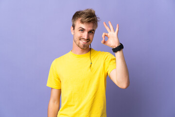 Young handsome blonde man isolated on purple background showing ok sign with fingers