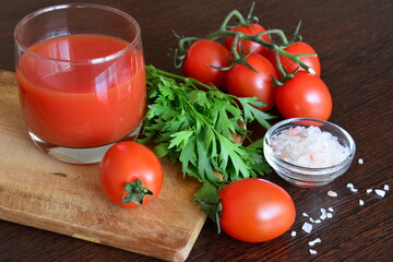 tomato juice in glasses with tomatoes, parsley, salad geens, pink salt on the cutting board on the wooden background