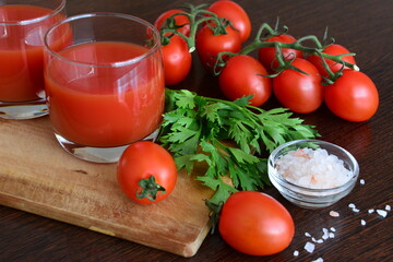 tomato juice in glasses with tomatoes, parsley, salad geens, pink salt on the cutting board on the wooden background