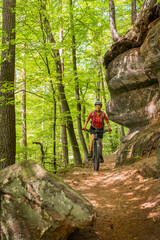 nice and active senior woman riding her electric mountain bike with full concentration on a rocks trail in the Pfaelzerwald forest near the city of Pirmasens in Rheinland-Pfalz, Germany
