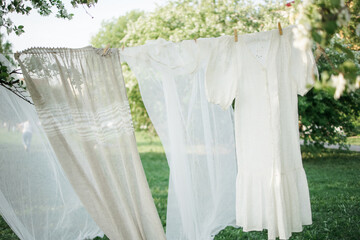 a white dress and curtains hang from a clothesline. sunny day. The concept of spring flowering.