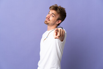 Young handsome blonde man isolated on purple background pointing front with happy expression