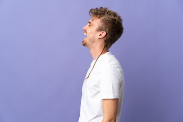 Young handsome blonde man isolated on purple background laughing in lateral position