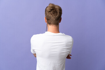 Young handsome blonde man isolated on purple background in back position