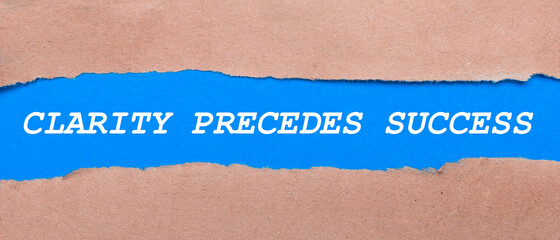 A strip of blue paper with the inscription CLARITY PRECEDES SUCCESS between the brown paper. View from above