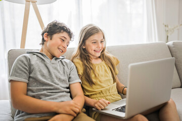 Fototapeta premium Youngs childrens using laptop on sofa in the living room at home