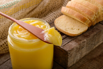 Ghee butter in glass jar with wooden spatula and sliced bread on wooden table.