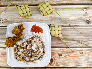 Flat lay image of a white rice with soy sauce and chili sauce with fried chicken and some ketupat isolated on a wooden background.