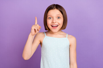 Photo of impressed brown hairdo small girl point up wear blue top isolated on violet color...