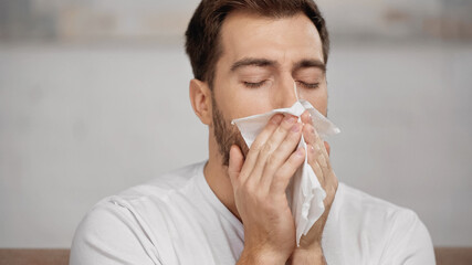 man with allergy sneezing in tissue at home