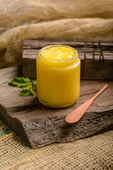 Ghee butter in glass jar with wooden spatula on wood.
