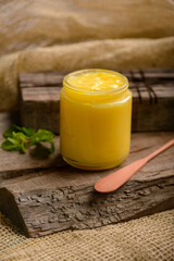 Ghee butter in glass jar with wooden spatula on wood.