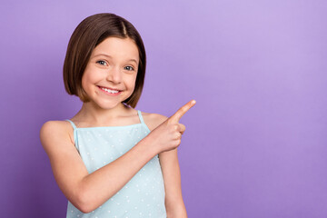 Photo of attractive young happy little girl point finger empty space sale news isolated on purple color background