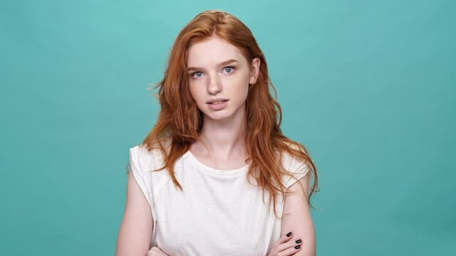 Carefree ginger woman in t-shirt listening something and showing her tongue over turquoise background