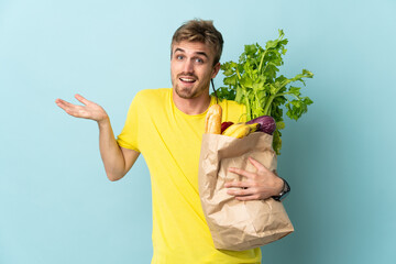 blonde Person taking a bag of takeaway food isolated on blue background with shocked facial...