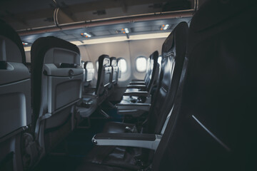 A dark interior of an aircraft: the row of modern empty thin leather seats with armrests down,...