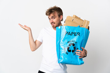 Young blonde man holding a recycling bag full of paper to recycle isolated on white background extending hands to the side for inviting to come