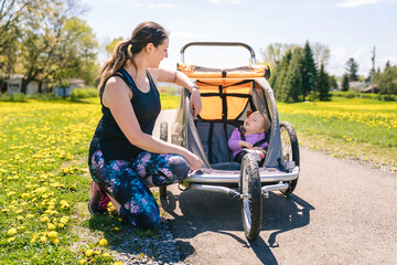 Beautiful young family with baby in jogging stroller running outside in summer season