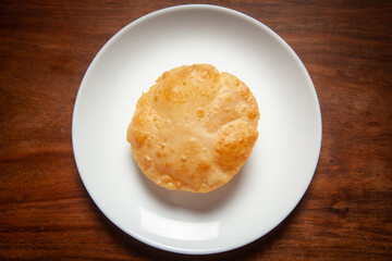Close-up of deep fried bhature (maida puri) made from  all purpose flour, served hot in white ceramic plate.