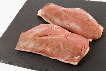 Two raw duck breast fillets on black slate plate
