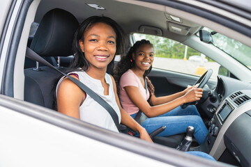 Young black teenage driver seated in her new car with her mother