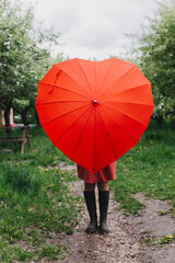 Pretty young woman hides behind heart shaped umbrella legs visible. Rain check