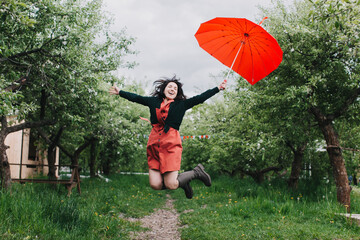 Pretty young woman carrying heart shaped umbrella and jumping in the garden. Having fun under the rain