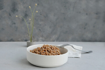 Bowl of buckwheat on a grey concrete background in minimalistic style. Concept of healthy food.