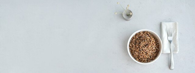 banner. Bowl of buckwheat on a grey concrete background in minimalistic style. Concept of healthy food.