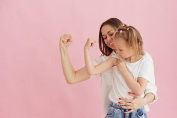 Funny family on the background of a bright pink wall. Mother and her daughter little girl having fun, showing that the strength of the muscles. Feminine power, feminism