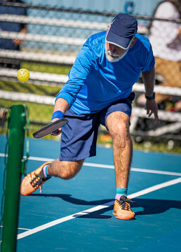 Senior man bends deeply for a dig shot in pickleball