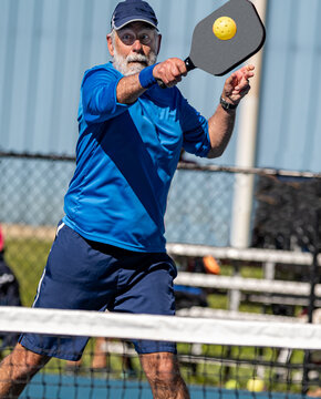 Senior man hits a hard volley in the game of pickleball