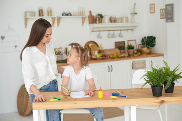 Tutor and child doing homework at kitchen. Mom and daughter are trying to solve the task. They are in a good mood and smile
