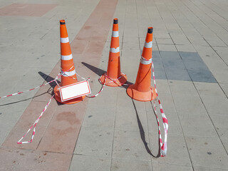 Plastic orange traffic sign in the form of a cone and red and white tape warns of danger