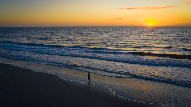 Woman takes picture of sunrise on beach.