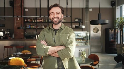 A handsome man is standing in the confident pose inside the cafe 