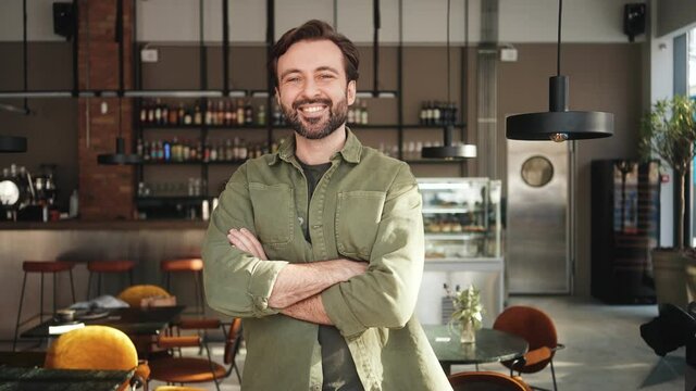 A handsome man is standing in the confident pose inside the cafe 