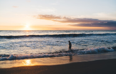 Silhouette of person walking into waving ocean