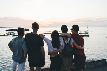 Unrecognizable friends admiring sunset on embankment