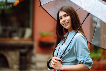 Young woman stands with umbrella in her hand on the street and looking into the camera. Smilling...