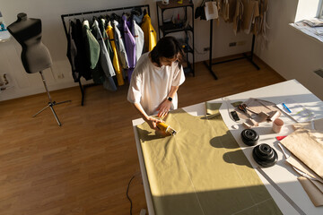 Sewing process: woman tailor working in shop with chalk patterns on fabric. Top angle view of young clothes designer cut textile for collection in fashion atelier studio. Dressmaking business owner