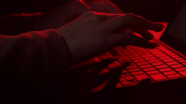 Hacker attack. Cyber security. Internet fraud. Web data protection. Unknown female programmer spy hands typing on laptop keyboard on dark red background.