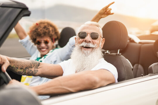 Happy senior multiracial couple having fun on road trip summer vacation inside convertible car