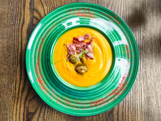 Pumpkin soup with mushrooms, bacon, microgreen on a green plate.