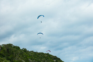 Paragliders taking off from a green mountain against a blue sky with clouds