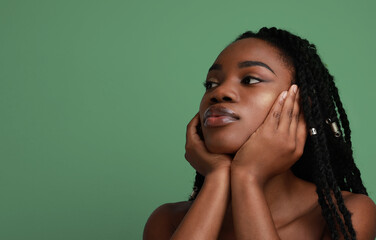 Thoughtful young black woman looking aside. Posing over green background.